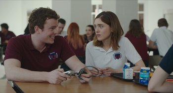 Movie still from “Yes, God, Yes” (2019), directed by Karen Maine – A man and a woman sitting at a wooden table; Medium shot, Over the shoulder angle