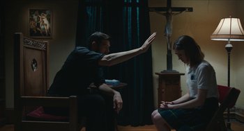 Movie still from “Yes, God, Yes” (2019), directed by Karen Maine – A man and a woman sitting in a living room; Medium shot, Over the shoulder angle