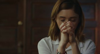 Movie still from “Yes, God, Yes” (2019), directed by Karen Maine – A woman with her hands clasped in front of her face; Close Up shot, Over the shoulder angle