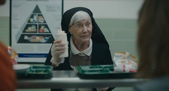 Movie still from “Yes, God, Yes” (2019), directed by Karen Maine – An older woman in a nun's outfit holding a bottle; Close Up shot, Over the shoulder angle