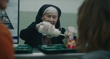 Movie still from “Yes, God, Yes” (2019), directed by Karen Maine – An older woman is eating food from a container; Close Up shot, Over the shoulder angle