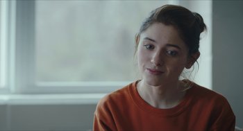 Movie still from “Yes, God, Yes” (2019), directed by Karen Maine – A young woman in an orange shirt looking at the camera; Close Up shot, Over the shoulder angle