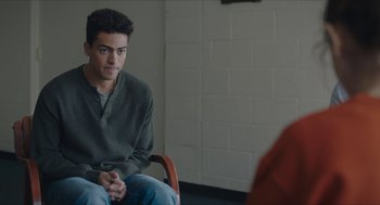 Movie still from “Yes, God, Yes” (2019), directed by Karen Maine – A man sitting in a chair in front of another man; Medium shot, Over the shoulder angle