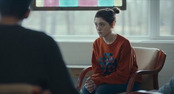 Movie still from “Yes, God, Yes” (2019), directed by Karen Maine – A woman sitting on a chair in front of a window; Medium shot, Over the shoulder angle