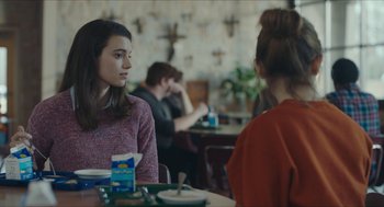 Movie still from “Yes, God, Yes” (2019), directed by Karen Maine – Two people sitting at a table in front of each other; Medium shot, Over the shoulder angle