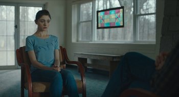 Movie still from “Yes, God, Yes” (2019), directed by Karen Maine – A woman sitting in a chair in front of a television; Medium shot, Over the shoulder angle