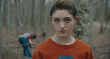 Movie still from “Yes, God, Yes” (2019), directed by Karen Maine – A woman in an orange shirt is looking at the camera; Close Up shot, Over the shoulder angle