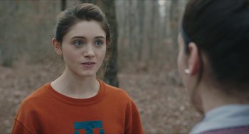 Movie still from “Yes, God, Yes” (2019), directed by Karen Maine – A young woman in an orange t - shirt talking to a man in the woods; Close Up shot, Over the shoulder angle