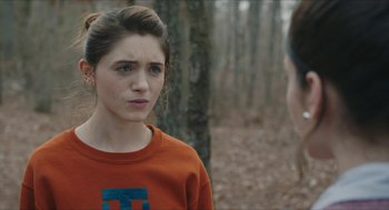 Movie still from “Yes, God, Yes” (2019), directed by Karen Maine – A young woman in an orange shirt talking to a man in the woods; Close Up shot, Over the shoulder angle