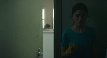 Movie still from “Yes, God, Yes” (2019), directed by Karen Maine – A woman holding a yellow cloth in a room; Medium shot, Over the shoulder angle