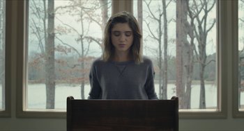 Movie still from “Yes, God, Yes” (2019), directed by Karen Maine – A woman sitting in front of a wooden desk; Medium shot, Over the shoulder angle