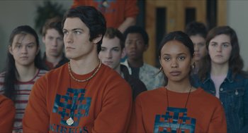 Movie still from “Yes, God, Yes” (2019), directed by Karen Maine – A man and a woman are standing in a room; Medium shot, Over the shoulder angle