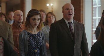 Movie still from “Yes, God, Yes” (2019), directed by Karen Maine – A group of people standing next to each other in a room; Medium shot, Over the shoulder angle