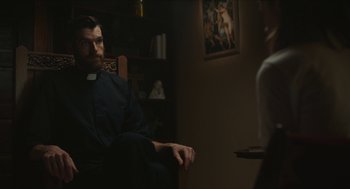 Movie still from “Yes, God, Yes” (2019), directed by Karen Maine – A man sitting in a chair in front of a woman; Medium shot, Over the shoulder angle