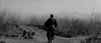 Movie still from “Yojimbo” (1961), directed by Akira Kurosawa – A man walking on a dirt path near a field; Wide shot, Low angle