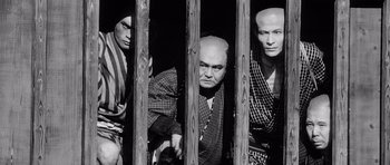 Movie still from “Yojimbo” (1961), directed by Akira Kurosawa – A group of men standing next to each other in front of a wooden fence; Medium shot, Low angle