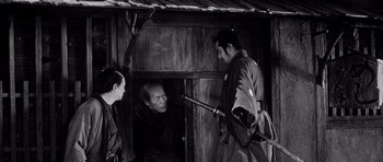 Movie still from “Yojimbo” (1961), directed by Akira Kurosawa – A man holding a katana in front of two other men; Medium shot, High angle