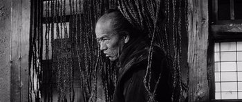 Movie still from “Yojimbo” (1961), directed by Akira Kurosawa – An older man standing in front of a bunch of ropes; Close Up shot, Low angle