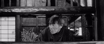 Movie still from “Yojimbo” (1961), directed by Akira Kurosawa – An old man with a long black hair and a bald head; Medium shot, Low angle