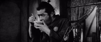 Movie still from “Yojimbo” (1961), directed by Akira Kurosawa – A man eating a bowl of food with chopsticks in his hands; Close Up shot, Low angle