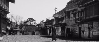Movie still from “Yojimbo” (1961), directed by Akira Kurosawa – A man standing in front of a building in an old town; Extreme Wide shot, Low angle
