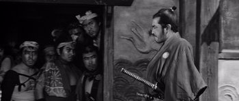 Movie still from “Yojimbo” (1961), directed by Akira Kurosawa – A black - and - white photo of a man holding a sword; Medium shot, Over the shoulder angle