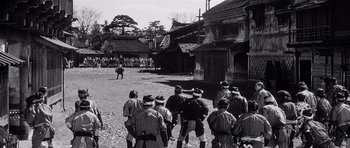 Movie still from “Yojimbo” (1961), directed by Akira Kurosawa – A black and white photo of a group of people in a village; Extreme Wide shot, Over the shoulder angle