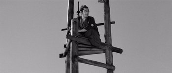 Movie still from “Yojimbo” (1961), directed by Akira Kurosawa – A man sitting on top of a wooden structure; Wide shot, Low angle