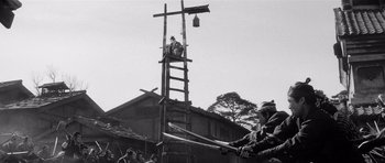 Movie still from “Yojimbo” (1961), directed by Akira Kurosawa – An old photo of a man holding a baseball bat on top of a ladder; Wide shot, Low angle