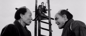 Movie still from “Yojimbo” (1961), directed by Akira Kurosawa – Two men talking to each other in front of a wooden ladder; Medium shot, Low angle