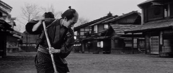Movie still from “Yojimbo” (1961), directed by Akira Kurosawa – A man holding a baseball bat while standing on a dirt field; Medium shot, Low angle