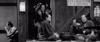 Movie still from “Yojimbo” (1961), directed by Akira Kurosawa – A man sitting on the ground next to another man; Wide shot, Over the shoulder angle