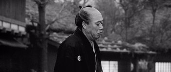 Movie still from “Yojimbo” (1961), directed by Akira Kurosawa – An older man with a bun and a black jacket; Close Up shot, Low angle