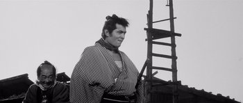 Movie still from “Yojimbo” (1961), directed by Akira Kurosawa – A black and white photo of a man in a kimono; Medium shot, Low angle