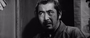 Movie still from “Yojimbo” (1961), directed by Akira Kurosawa – Black and white photograph of a man looking at the camera; Close Up shot, Low angle