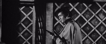 Movie still from “Yojimbo” (1961), directed by Akira Kurosawa – A black and white photo of a man holding two guns; Medium shot, Low angle
