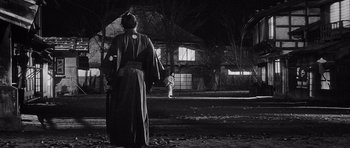 Movie still from “Yojimbo” (1961), directed by Akira Kurosawa – A man in a robe stands in front of a building; Extreme Wide shot, Low angle