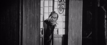 Movie still from “Yojimbo” (1961), directed by Akira Kurosawa – An old photo of a man smoking a cigarette in front of a window; Medium shot, Low angle