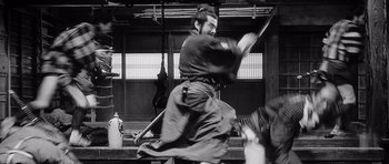 Movie still from “Yojimbo” (1961), directed by Akira Kurosawa – A man in a samurai garb swinging a sword; Medium shot, Low angle