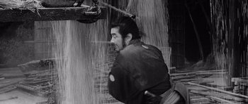 Movie still from “Yojimbo” (1961), directed by Akira Kurosawa – A black and white photo of a man in the rain; Medium shot, Low angle