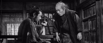 Movie still from “Yojimbo” (1961), directed by Akira Kurosawa – A man sitting next to another man holding a cup; Medium shot, Over the shoulder angle