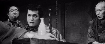 Movie still from “Yojimbo” (1961), directed by Akira Kurosawa – A man holding two vases and a sword in his hands; Medium shot, Low angle