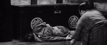 Movie still from “Yojimbo” (1961), directed by Akira Kurosawa – A man is lying on the ground next to an open trunk; Wide shot, High angle