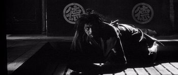 Movie still from “Yojimbo” (1961), directed by Akira Kurosawa – A man with dreadlocks sitting in a dark room; Wide shot, High angle