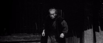 Movie still from “Yojimbo” (1961), directed by Akira Kurosawa – An old man wearing a black robe and a black mask; Medium shot, High angle