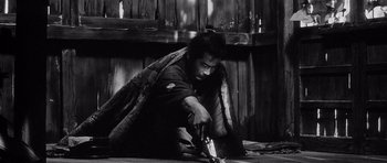 Movie still from “Yojimbo” (1961), directed by Akira Kurosawa – Black and white photograph of a man holding a bottle; Medium shot, High angle