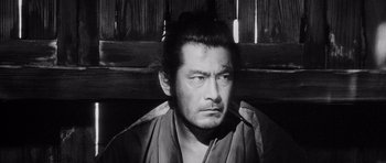 Movie still from “Yojimbo” (1961), directed by Akira Kurosawa – A man with a long hair and a beard is looking at the camera; Close Up shot, High angle