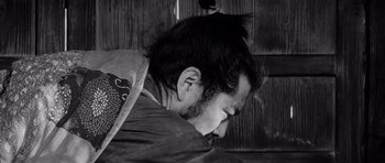 Movie still from “Yojimbo” (1961), directed by Akira Kurosawa – A man with long black hair is sleeping; Close Up shot, Low angle