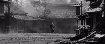 Movie still from “Yojimbo” (1961), directed by Akira Kurosawa – A man walking on a dirt road near a building; Extreme Wide shot, High angle