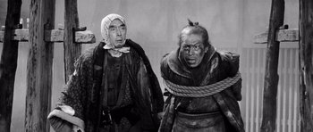 Movie still from “Yojimbo” (1961), directed by Akira Kurosawa – Two men are tied to a rope and one is wearing a hat; Medium shot, High angle